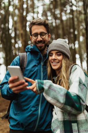 Cheerful young caucasian couple in jackets in forest enjoy travel vacation, use smartphone app map