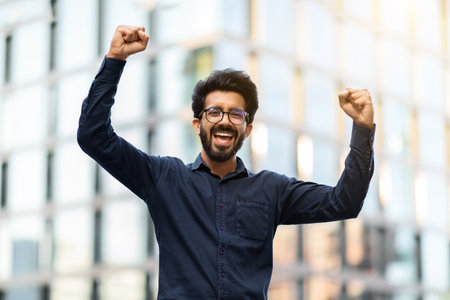 Happy young indian businessman raising hands up on the streetの写真素材