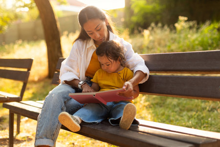 Korean Mom and Baby Daughter Sharing Reading Moment At Parkの写真素材