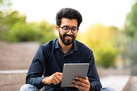 Happy young indian man hipster using digital tablet on streetの写真素材
