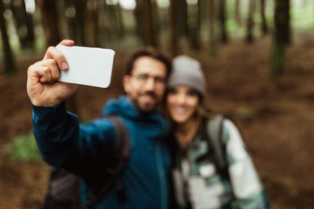 Positive young caucasian guy and lady in jackets enjoy travel vacation, make selfie on smartphoneの写真素材