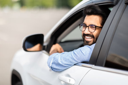 Happy young indian man driver sitting inside white luxury car