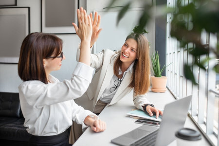 Corporate celebration. United two businesswomen giving high five celebrating business success together in officeの写真素材