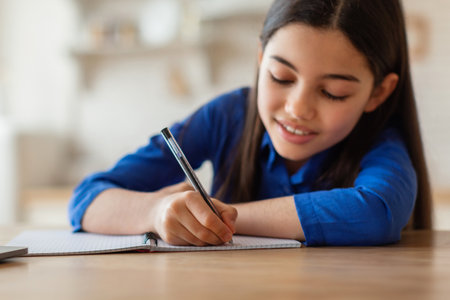 Smiling schoolgirl writing or drawing in paper notebook at home