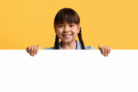 Cute little asian girl kid posing behind blank advertising board