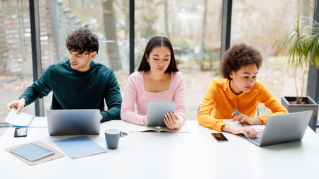 Multiracial students sitting in university audience, using various gadgets, learning for exams indoorsの写真素材