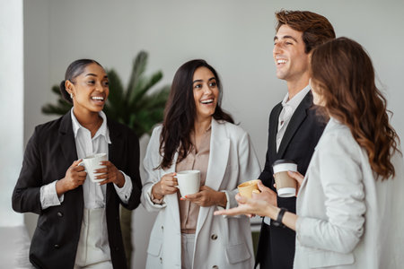 Group of multiethnic colleagues standing with cups of coffee and talking while taking coffee break, office interiorの写真素材