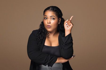 Surprised brazilian body positive lady having creative idea, experiencing AHA moment on brown studio...