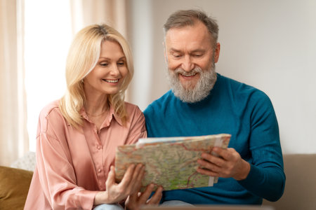Cheerful Senior Couple Holding Paper Travel Map, Planing Vacation Indoorの写真素材