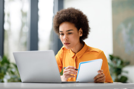 Remote education. Focused latin lady watching video course on laptop and taking notes, learning virtual lessonの写真素材