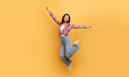 Carefree asian lady jumping in air and smiling, happy japanese woman having fun over yellow background, full lengthの写真素材