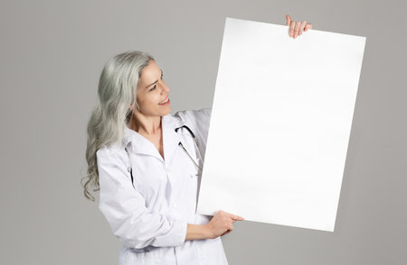 Lady Doctor Showing Blank Paper Poster Over Gray Studio Backgroundの写真素材