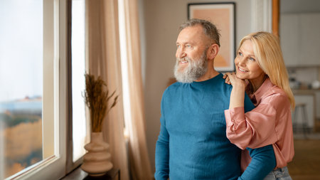 Loving Senior Spouses Standing Looking From Window At Home, Panorama