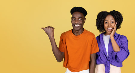 Positive surprised millennial black couple in casual point hand on empty spaceの写真素材
