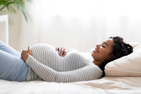 Awaiting Baby. Happy Black Pregnant Woman Touching Belly While Lying On Bedの写真素材