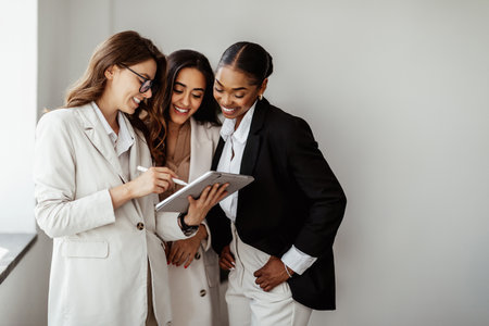 Happy multiracial businesswomen using modern digital tablet, discussing new ideas and projects in office, free spaceの写真素材