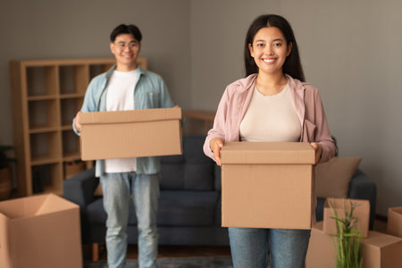 Young Asian Spouses Holding Cardboard Boxes Happy About Moving Indoor