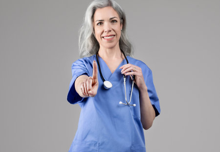 Smiling nurse woman pointing finger up having advice, gray backgroundの写真素材