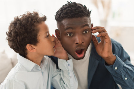 Little son whispering rumors and news in dad ear indoorsの写真素材