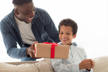 African dad giving gift box to little son at homeの写真素材