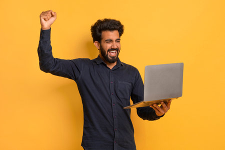 Joyful Young Indian Man Holding Laptop And Celebrating Successの写真素材