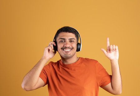 Joyful brazilian man listening to music and smiling, raising finger up, touching his brand wireless headset, copy spaceの写真素材