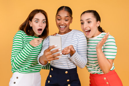 Excited multiracial ladies looking at smartphone screen and exclaimingの写真素材