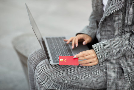 Unrecognizable Woman Using Laptop Computer And Credit Card Sitting Outdoorの写真素材