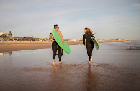 Two Surfers Man And Woman Walking With Surfboards Along The Beach