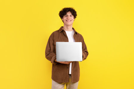 Smart student guy with laptop using computer over yellow backgroundの写真素材