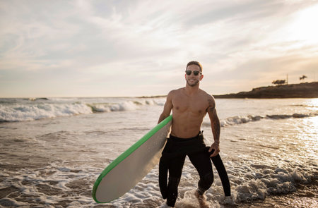 Young Athletic Surfer Man In Wetsuit Walking With Surfboard On The Beachの写真素材
