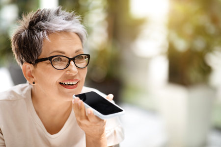 Closeup of mature businesswoman recording voice mail on smartphoneの写真素材