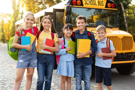 Group Of Happy Kids With Workbooks Standing Outdoors Near School Busの写真素材