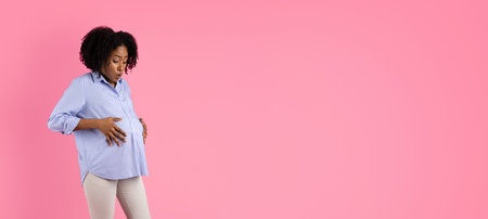 Despaired shocked millennial black pregnant lady with big belly suffering from pain and contractionsの写真素材