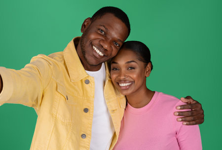 Happy attractive black couple taking selfie, cuddling on colorful backgroundの写真素材