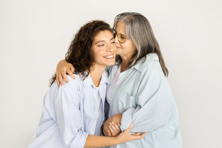 Positive caucasian old woman kiss in cheek millennial lady, enjoy love and support on white wall backgroundの写真素材