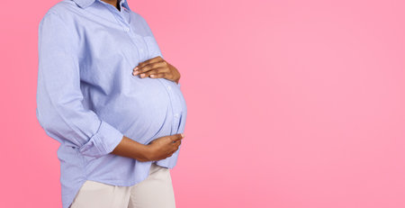 Millennial black pregnant lady touch belly with hands, enjoy motherhood, isolated on pink backgroundの写真素材