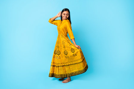 Young Indian Lady Wearing Yellow Traditional Dress Dancing, Blue Background