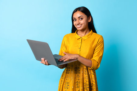 Indian Woman Using Laptop Posing In Traditional Dress, Blue Backgroundの写真素材