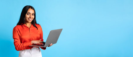 Happy Indian Lady Holding Laptop Browsing Internet On Blue Backgroundの写真素材