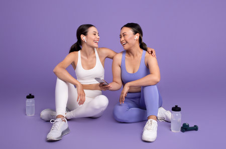 App for body care. Happy diverse female friends sitting on floor, talking, relaxing after training on purple backgroundの写真素材