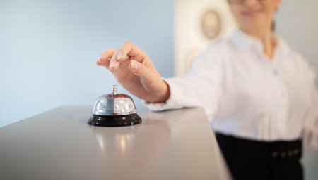 Unrecognizable Businesswoman Pushing Call Bell At Reception Counter Standing Indoors