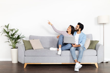 Happy loving indian couple thinking on interior design, using laptopの写真素材