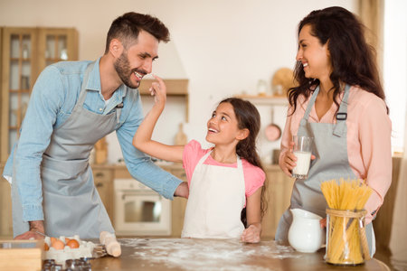 Excited child girl playing with floor and dad while baking with parents together in kitchenの写真素材