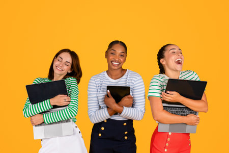 Thrilled young multiracial women hugging gadgets, yellow backgroundの写真素材