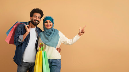 Great Offer. Excited young arab couple with bright shopping bags pointing asideの写真素材