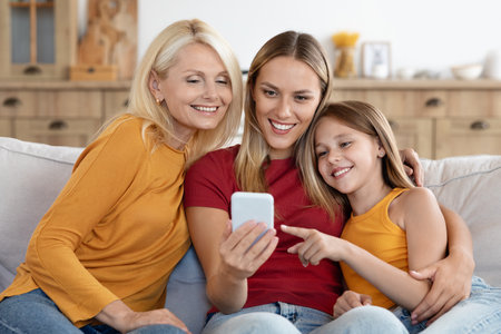 Cheerful loving family mother, daughter, granny using phone at homeの写真素材