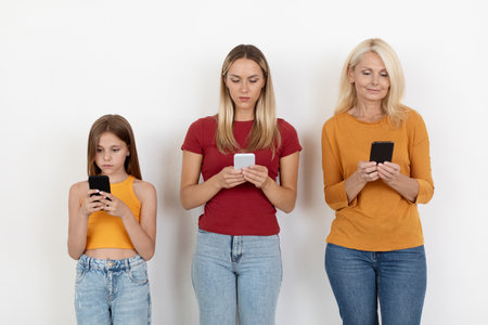 Mother, daughter, grandmother holding phones while posing on white background