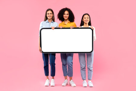 Full length shot of diverse ladies holding huge smartphone with white blank screen, offering mockup...