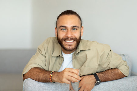 Cheerful millennial man holding glass of water, home interiorの写真素材